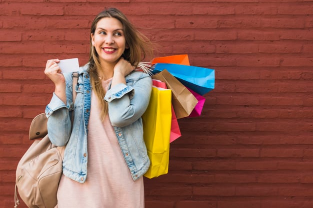 Mulher feliz que está com sacos de compras e cartão de crédito na parede de  tijolo vermelho | Foto Grátis